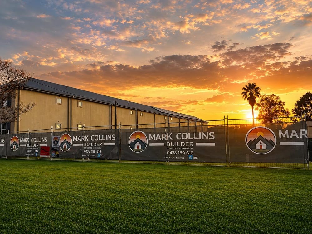 Mark Collins Builder branded site fencing at a commercial project at sunset